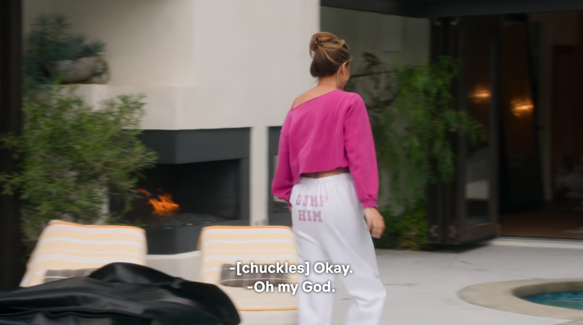Chrishell Stause walking by her pool wearing white sweatpants that say DUMP HIM in pink rhinestones on the butt